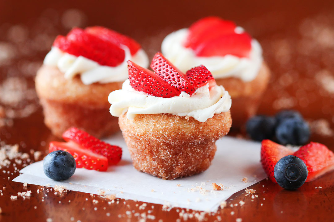 Strawberry Shortcake Doughnut Muffins. These are like little bites of HEAVEN. A muffin that tastes like a doughnut, dunked in brown butter and rolled in cinnamon sugar for a sweet, crunchy crust. Then topped with buttercream frosting and fresh cut strawberries. Amazing.