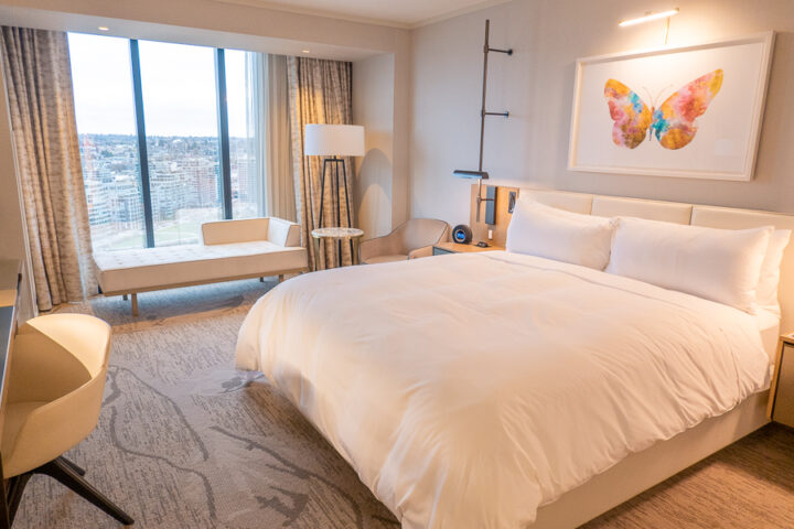 hotel bed on a high floor with floor to ceiling windows and city view