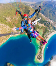 Two girls tandem paragliding over a turquoise blue lagoon and beach