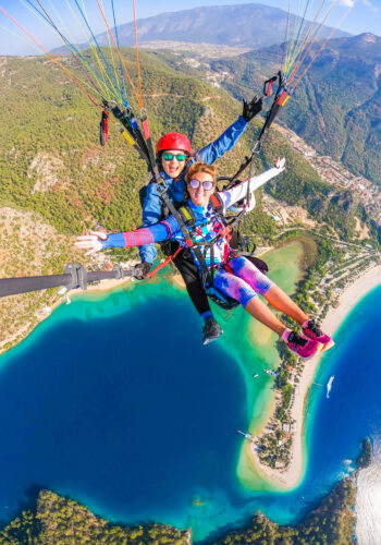 Two girls tandem paragliding over a turquoise blue lagoon and beach