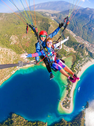 Two girls tandem paragliding over a turquoise blue lagoon and beach