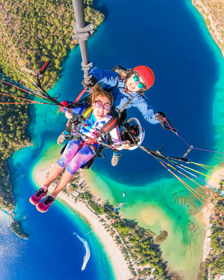 Top down view of Two girls tandem paragliding over a turquoise blue lagoon and beach